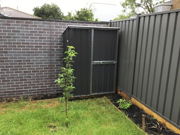 Slim garden shed against a brick wall.